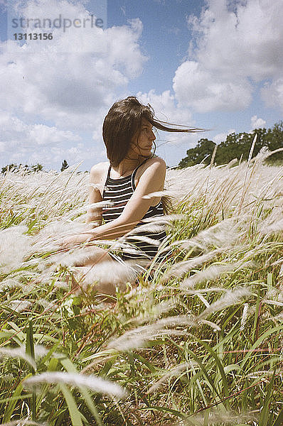 Frau sitzt bei windigem Wetter auf dem Feld gegen den Himmel
