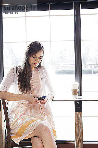 Frau benutzt Mobiltelefon  während sie im Café sitzt