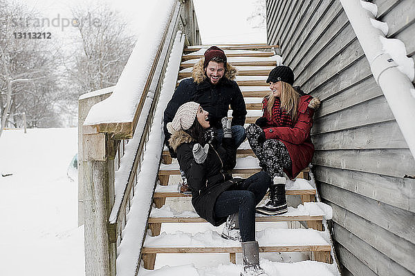 Glückliche Freunde unterhalten sich  während sie auf schneebedeckten Stufen sitzen