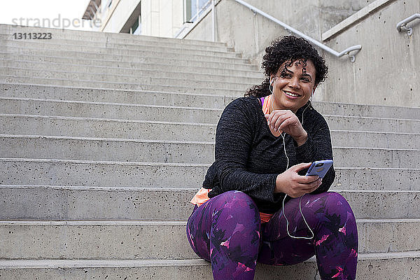 Niedriger Blickwinkel einer Frau  die über ein Mobiltelefon Musik hört  während sie auf einer Treppe sitzt