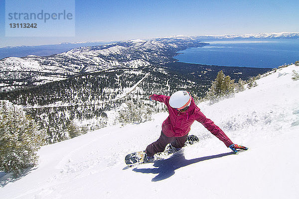 Hochwinkelaufnahme einer Snowboarderin beim Abstieg vom schneebedeckten Berg