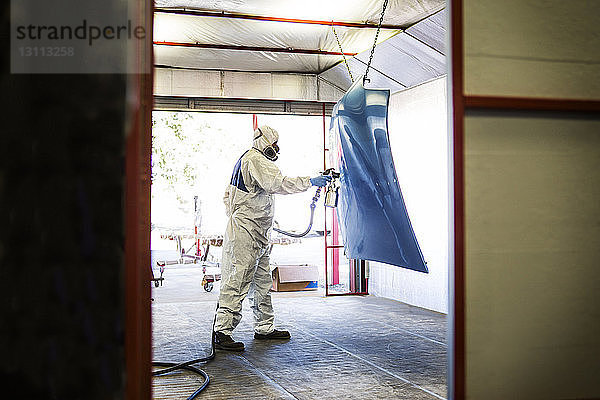 Mechaniker für Arbeitsschutzkleidung beim Lackieren von Fahrzeugteilen in der Karosseriewerkstatt