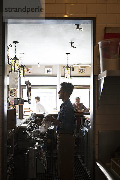 Seitenansicht des Eigentümers  der Gläser an der Bartheke von Kunden im Cafe reinigt