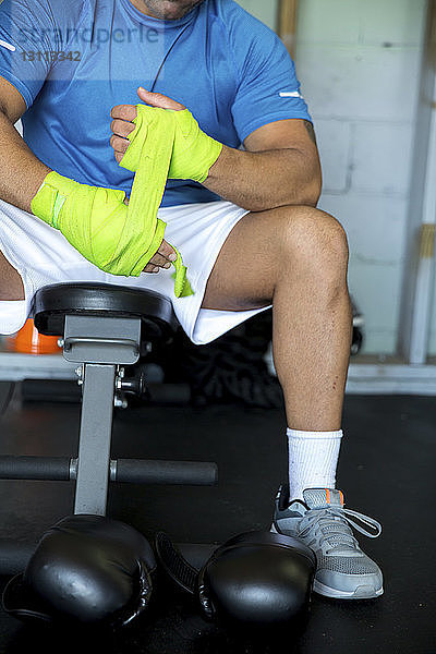 Niedriger Abschnitt eines männlichen Boxers  der beim Sitzen im Fitnessstudio Armbänder bindet