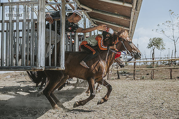Mann führt Kinderjockey auf Rennpferd beim Pferderennen am Starttor