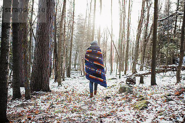 Rückansicht einer Frau mit Decke beim Waldspaziergang im Algonquin-Provinzpark im Winter