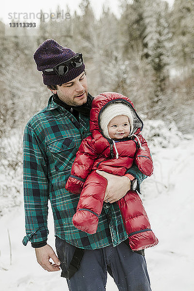 Vater trägt süße Tochter  während er im Winter im Wald steht