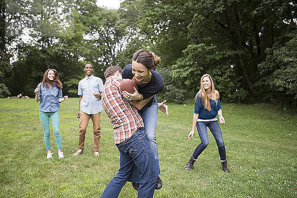 Mann verteidigt Frau mit Fussball in der Hand  während Freunde sie auf dem Feld beobachten