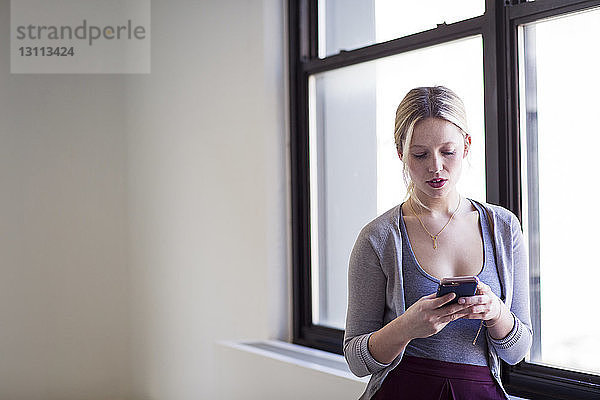 Geschäftsfrau benutzt Mobiltelefon am Fenster im neuen Büro