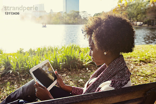 Frau benutzt Tablette  während sie an einem sonnigen Tag auf einer Parkbank sitzt