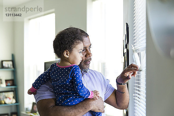 Vater und Tochter schauen zu Hause durch Fensterläden