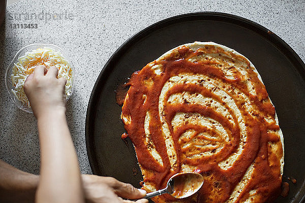 Beschnittenes Bild von Vater und Tochter beim Auftragen von Soße auf Pizzabrot