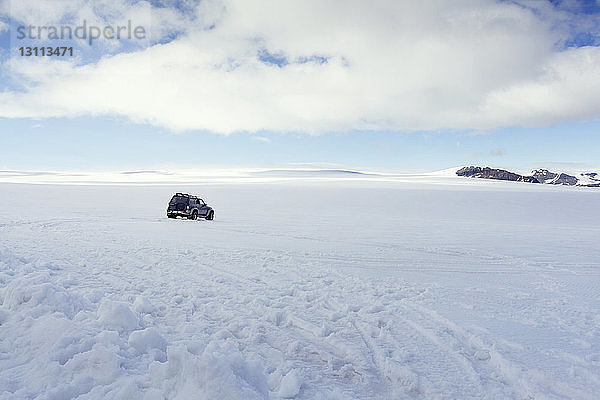 Auto auf schneebedeckter Landschaft vor bewölktem Himmel