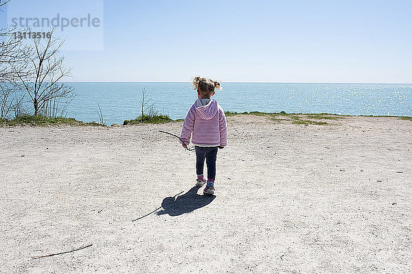 Rückansicht eines Mädchens  das auf einer Klippe am Meer vor klarem Himmel geht