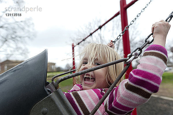 Porträt eines glücklichen Mädchens  das sich auf einem Spielplatz gegen den Himmel schwingt