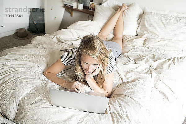 Hochwinkelansicht einer Frau  die einen Laptop-Computer benutzt  während sie sich im Bett entspannt