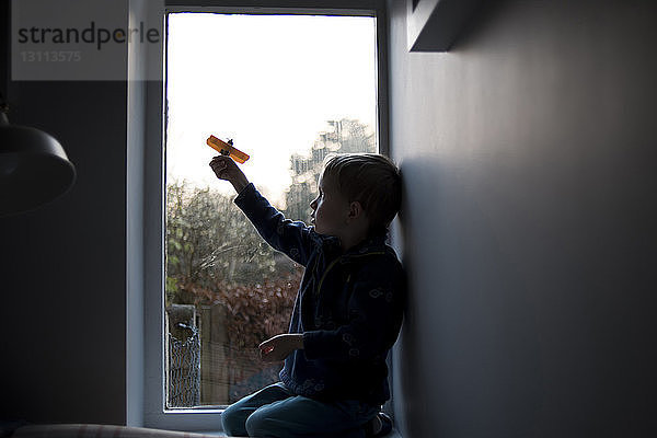 Junge spielt mit Spielzeug  während er zu Hause am Fenster kniet