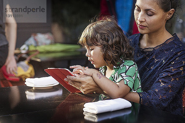 Mutter und Tochter benutzen Tablet-Computer im Straßencafé