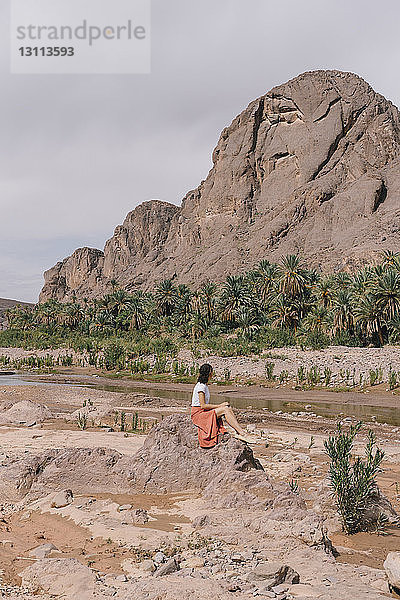 Seitenansicht einer auf einem Felsen sitzenden Frau vor bewölktem Himmel