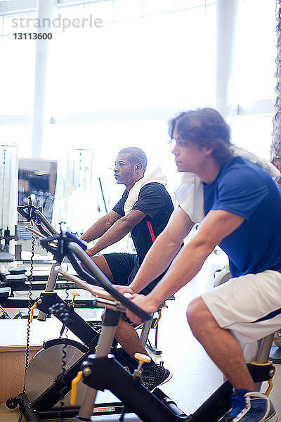 Seitenansicht von Männern auf Heimtrainern im Fitnessstudio