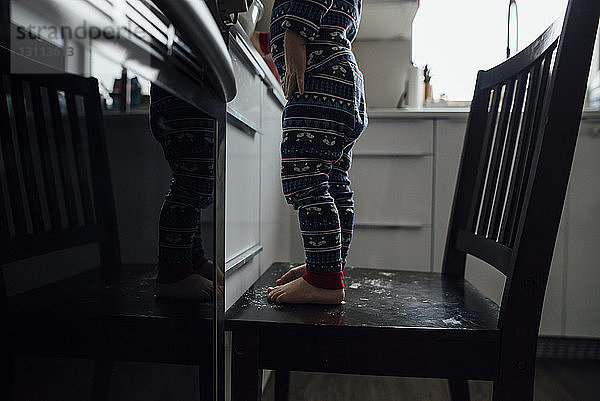 Niedriger Teil eines kleinen Jungen  der zu Hause in der Küche auf einem Stuhl steht