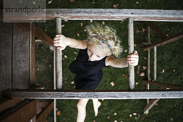 Draufsicht auf ein sorgloses Mädchen  das auf einem Spielplatz an Affenstangen hängt