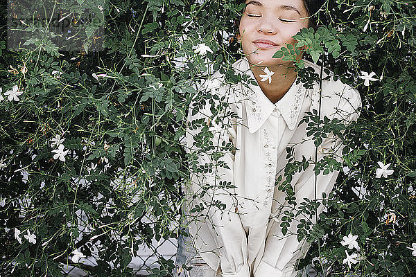 Entspannte Frau steht mit geschlossenen Augen inmitten von Pflanzen im Hinterhof