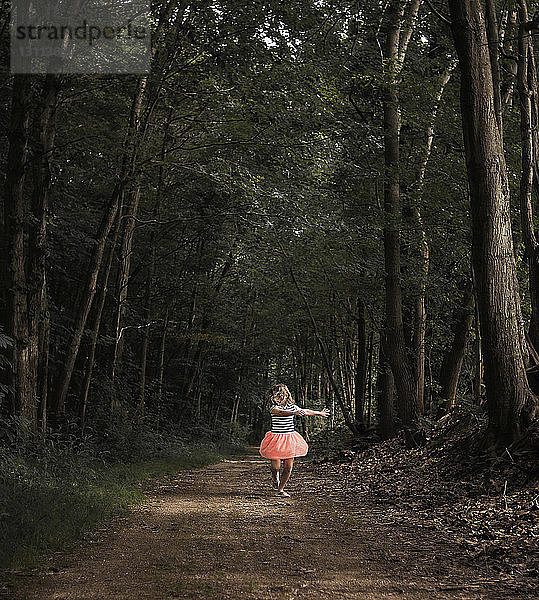 Mädchen tanzt auf Feldweg inmitten von Wald