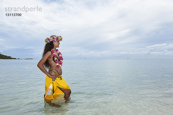 Frau in traditioneller Kleidung steht im Meer vor bewölktem Himmel