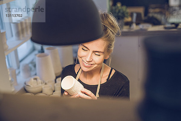 Hochwinkelansicht einer lächelnden Frau  die Keramik hält  während sie in einem Workshop steht