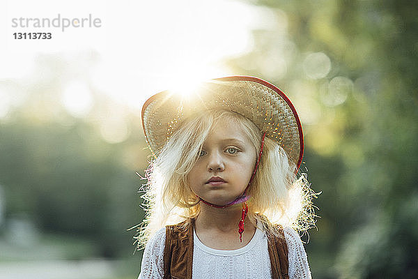 Porträt eines Mädchens mit Sonnenhut  das an einem sonnigen Tag im Park steht