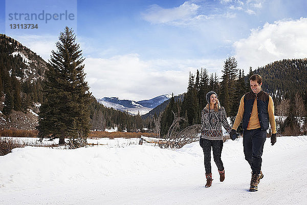Glückliches Paar hält sich an den Händen  während es auf verschneitem Feld gegen den Himmel läuft