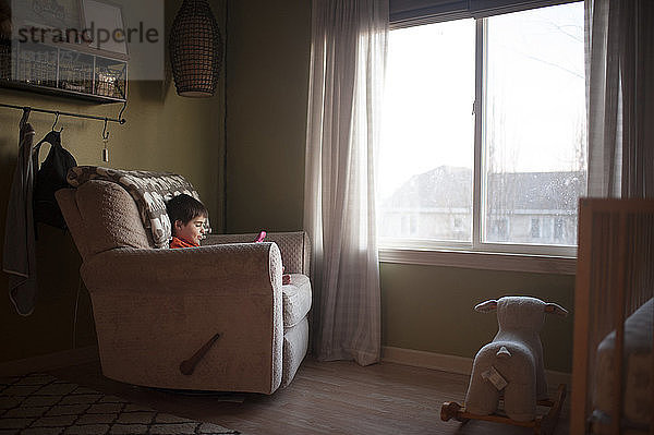 Junge spielt mit Spielzeug  während er zu Hause auf einem Stuhl am Fenster sitzt