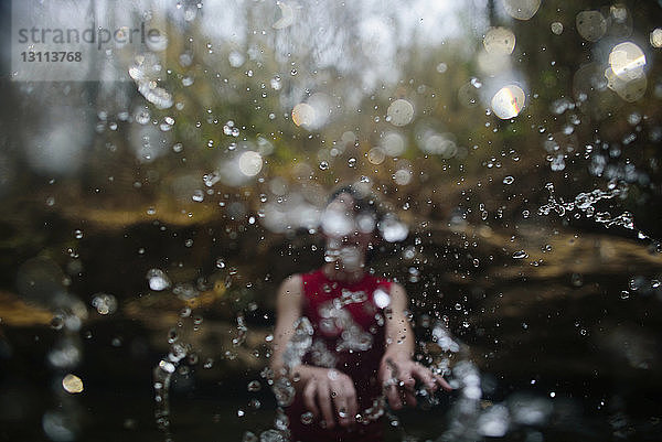 Junge  der beim Spielen im Fluss Wasser spritzt