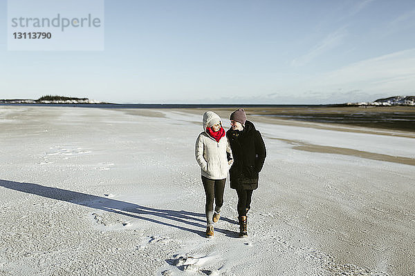 Freundinnen in voller Länge  die im Winter auf verschneitem Feld gegen den Himmel laufen
