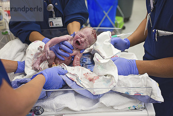 Mittelteil eines hemdlosen Vaters mit neugeborenem Sohn im Krankenhaus im Bett liegend