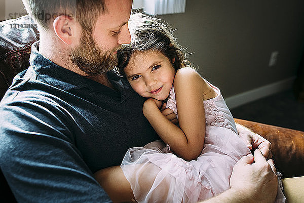 Porträt eines Mädchens mit Vater zu Hause auf dem Sofa sitzend