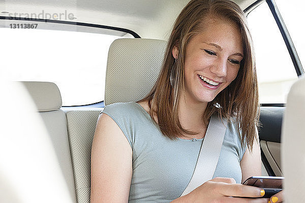 Glücklicher Teenager  der im Auto sitzend ein Mobiltelefon benutzt