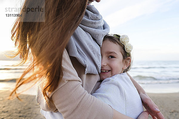 Porträt einer glücklichen Tochter  die ihre Mutter umarmt  während sie bei Sonnenuntergang am Strand steht