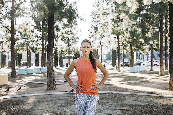 Porträt einer selbstbewussten Sportlerin  die mit den Händen auf der Hüfte im Park steht