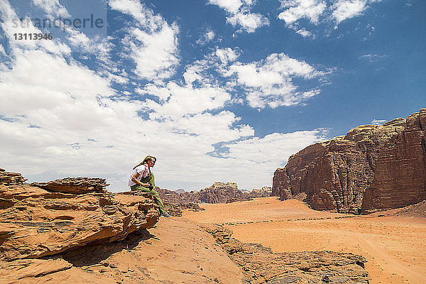 Frau sitzt an einem sonnigen Tag auf einem Felsen gegen den Himmel