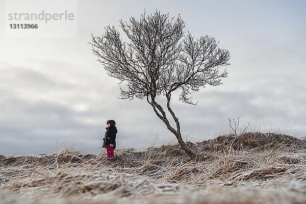 Mädchen steht am kahlen Baum gegen den Himmel auf dem Feld