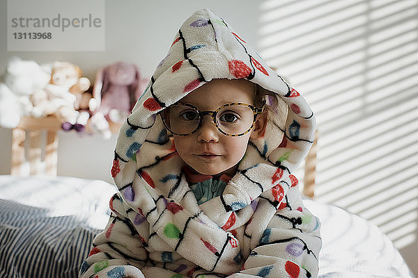 Bildnis eines Mädchens in warmer Kleidung  das zu Hause auf dem Bett sitzt