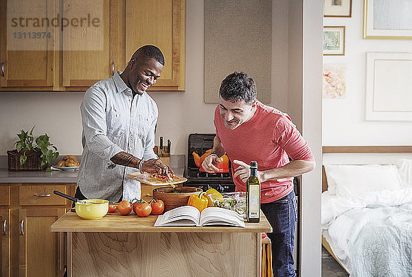 Glückliches multiethnisches schwules Paar bereitet zu Hause in der Küche Essen zu