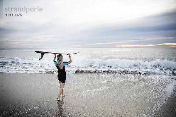 Rückansicht einer Surferin  die ein Surfbrett auf dem Kopf trägt  während sie am Strand von Delray in Richtung Meer läuft