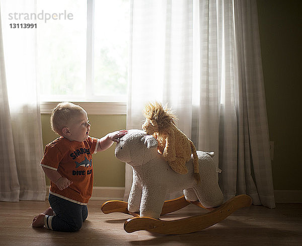 Kleiner Junge spielt mit Lammwippe  während er zu Hause auf dem Boden kniet