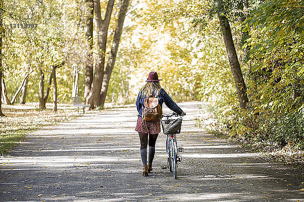 Rückansicht einer Frau mit Fahrrad auf einer Straße inmitten von Bäumen