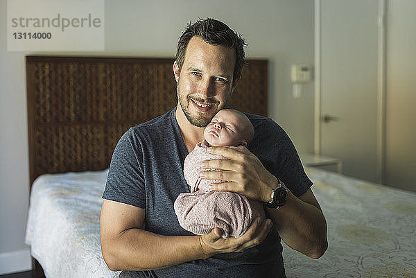 Porträt eines glücklichen Vaters  der seine neugeborene Tochter im Schlafzimmer trägt