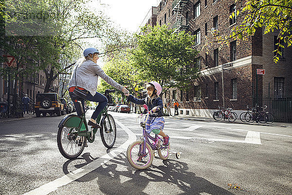 Mutter und Tochter geben High-Five  während sie auf der Straße Fahrrad fahren