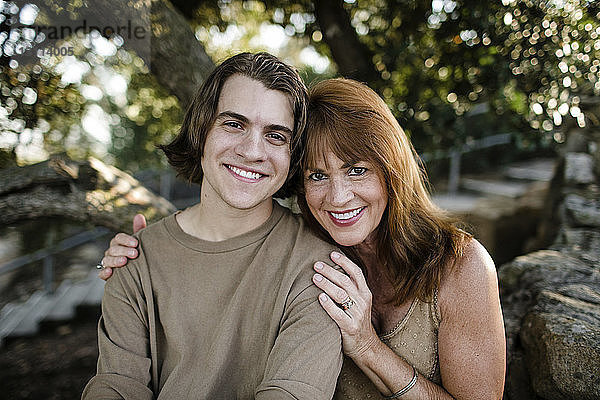 Porträt einer glücklichen Mutter mit Sohn an Bäumen sitzend im Park